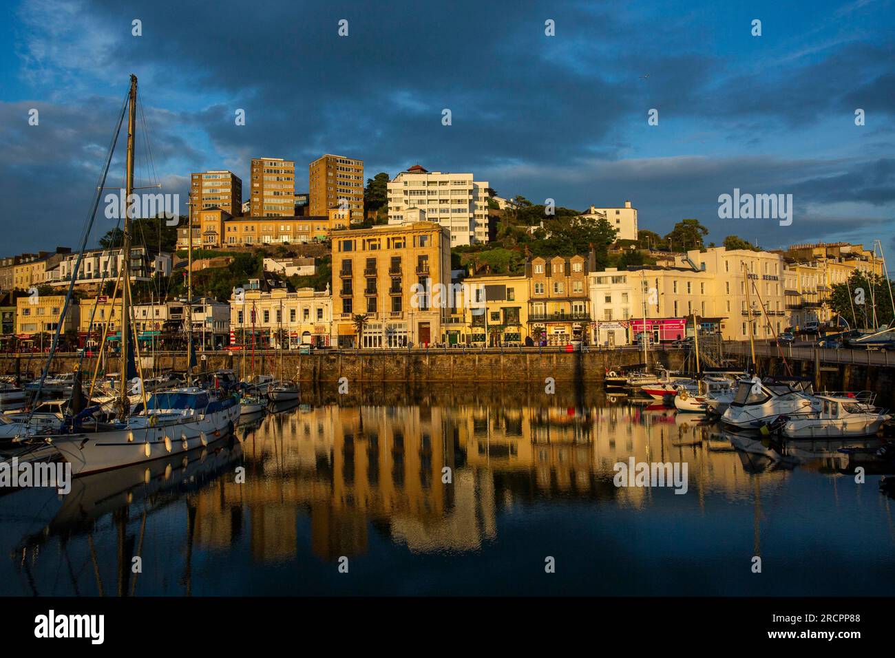 Eine Reihe verschiedener Gebäude mit Blick auf den Hafen von Torquay erhalten einen warmen Sonnenuntergang. Stockfoto