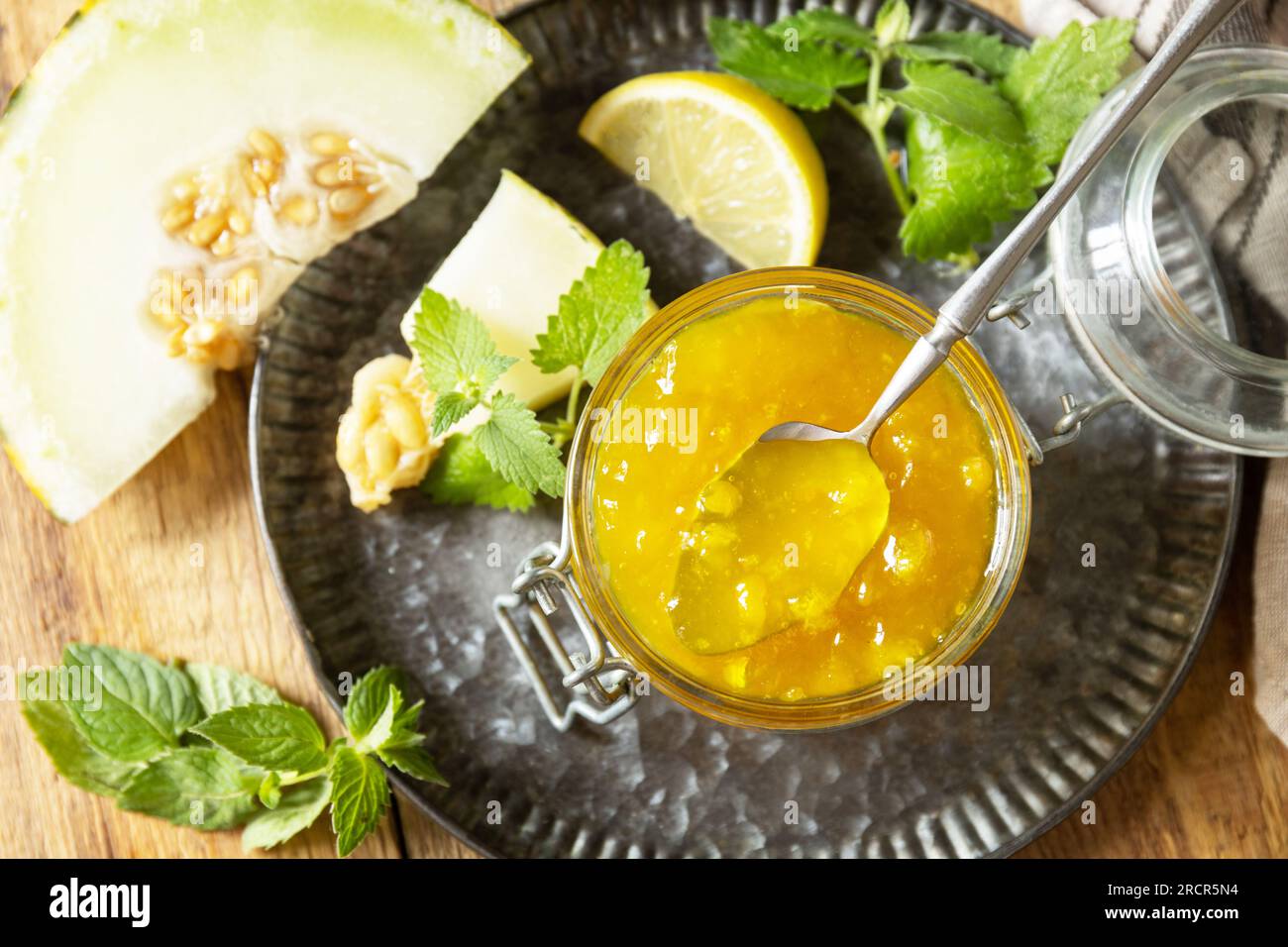 Hausgemachtes Preserve. Süße Melone und Zitrusmarmelade oder Gelee in einem kleinen Glasgefäß mit frischen Melonenscheiben auf einem rustikalen Holztisch. Blick von oben. Stockfoto