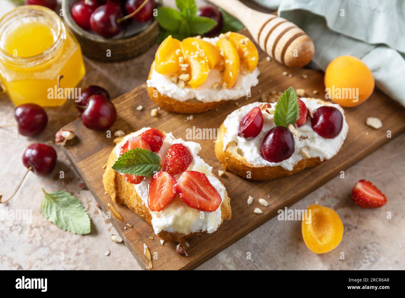 Sandwich mit Kirsche, Erdbeeren, Weichkäse und Honig auf Holzbrett auf Steinhintergrund. Beeren Toast Frühstück, gesundes Essen. Stockfoto