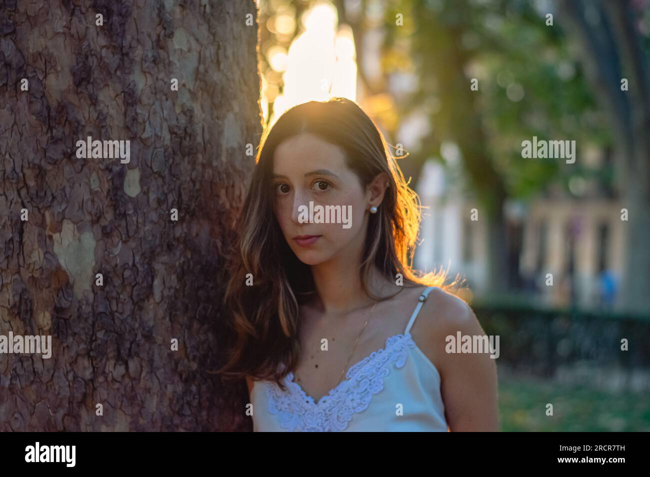 Horizontale Nahaufnahme einer hübschen jungen Frau, die neben einem Baum steht und in die Kamera schaut Stockfoto