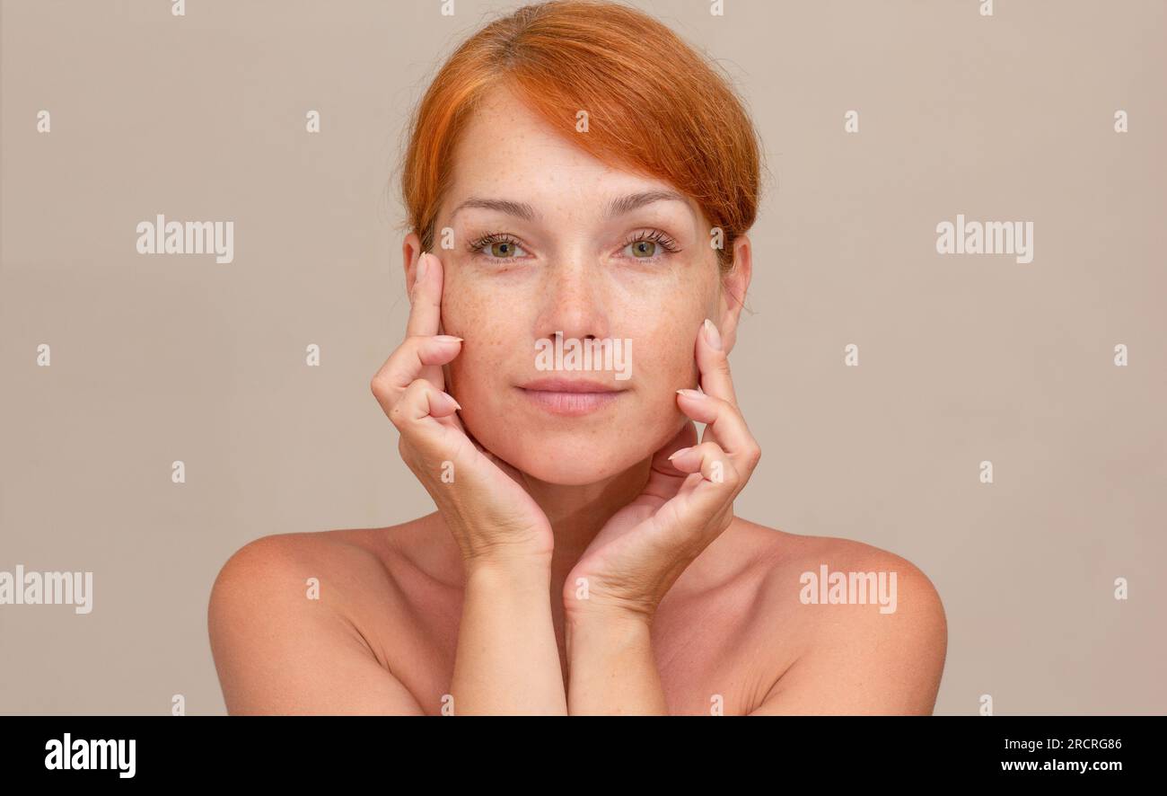 Porträt einer weißhäutigen Frau mittleren Alters im Alter von 40s Jahren mit rötlichen Haaren, die auf die Kamera blickt, Finger auf der Wange hält und weiche Haut zeigt Stockfoto