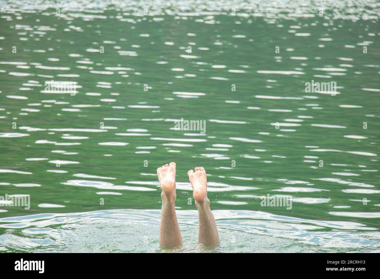 Männerbeine stehen in einem Steinbruch in der Ukraine während des Schwimmens, der Füße im Wasser, des Ertrinkens, des Sommers aus dem Wasser Stockfoto