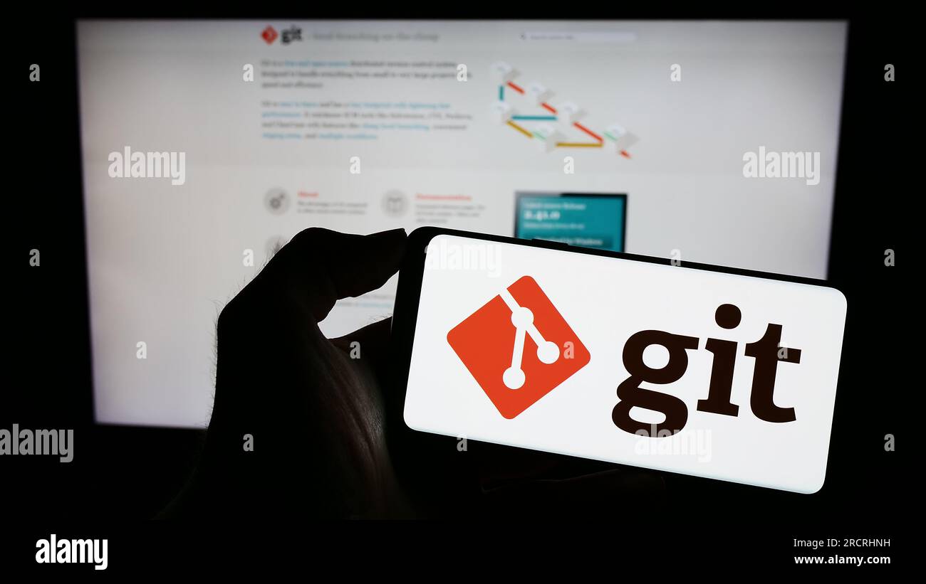 Person, die ein Mobiltelefon mit dem Logo des verteilten Versionskontrollsystems Git auf dem Bildschirm vor der Webseite hält. Konzentrieren Sie sich auf das Display des Telefons. Stockfoto