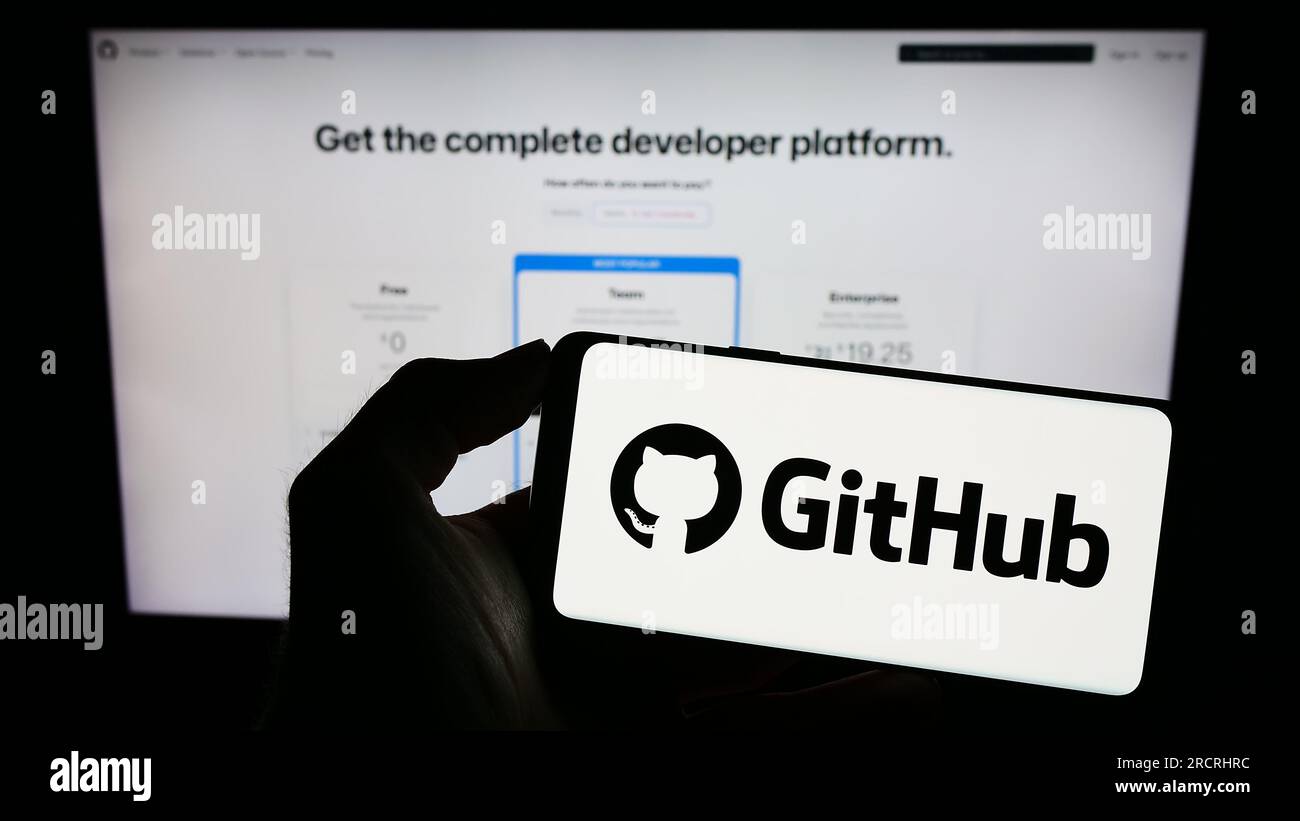 Person, die ein Mobiltelefon mit dem Logo des US-Softwareentwicklungsunternehmens GitHub Inc. Auf dem Bildschirm vor der Unternehmenswebseite hält. Konzentrieren Sie sich auf das Display des Telefons. Stockfoto