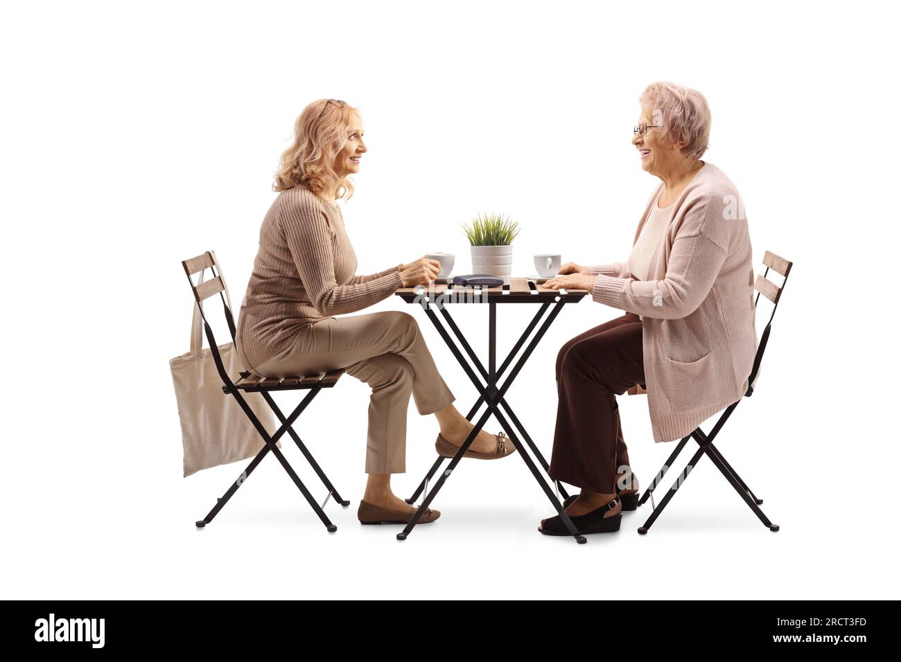 Ältere und jüngere Frau, die an einem Tisch sitzt und eine Tasse Kaffee trinkt, isoliert auf weißem Hintergrund Stockfoto