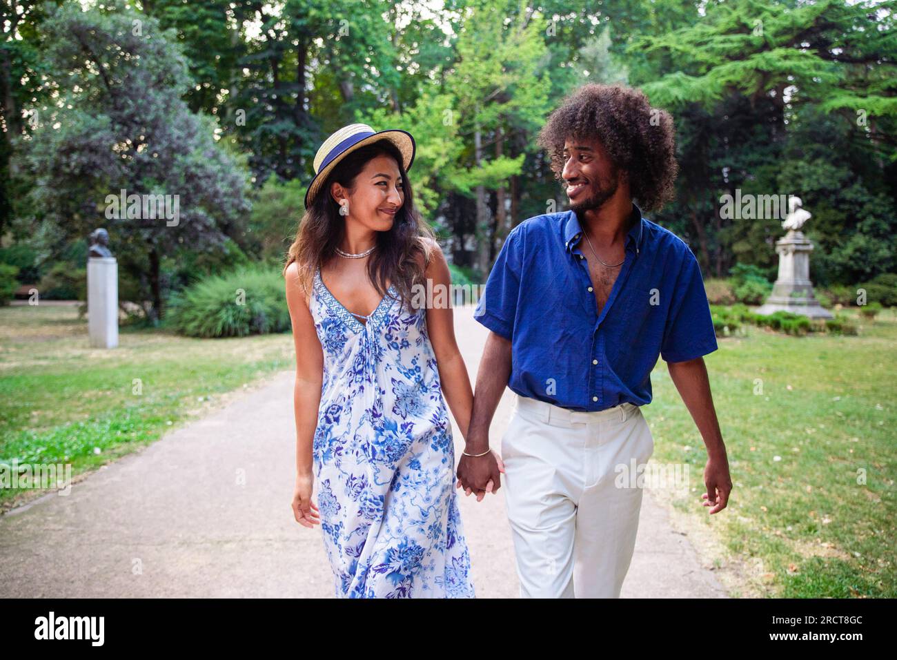 Ein multiethnisches Paar spaziert im Sommer in einem öffentlichen Park und hält Händchen Stockfoto