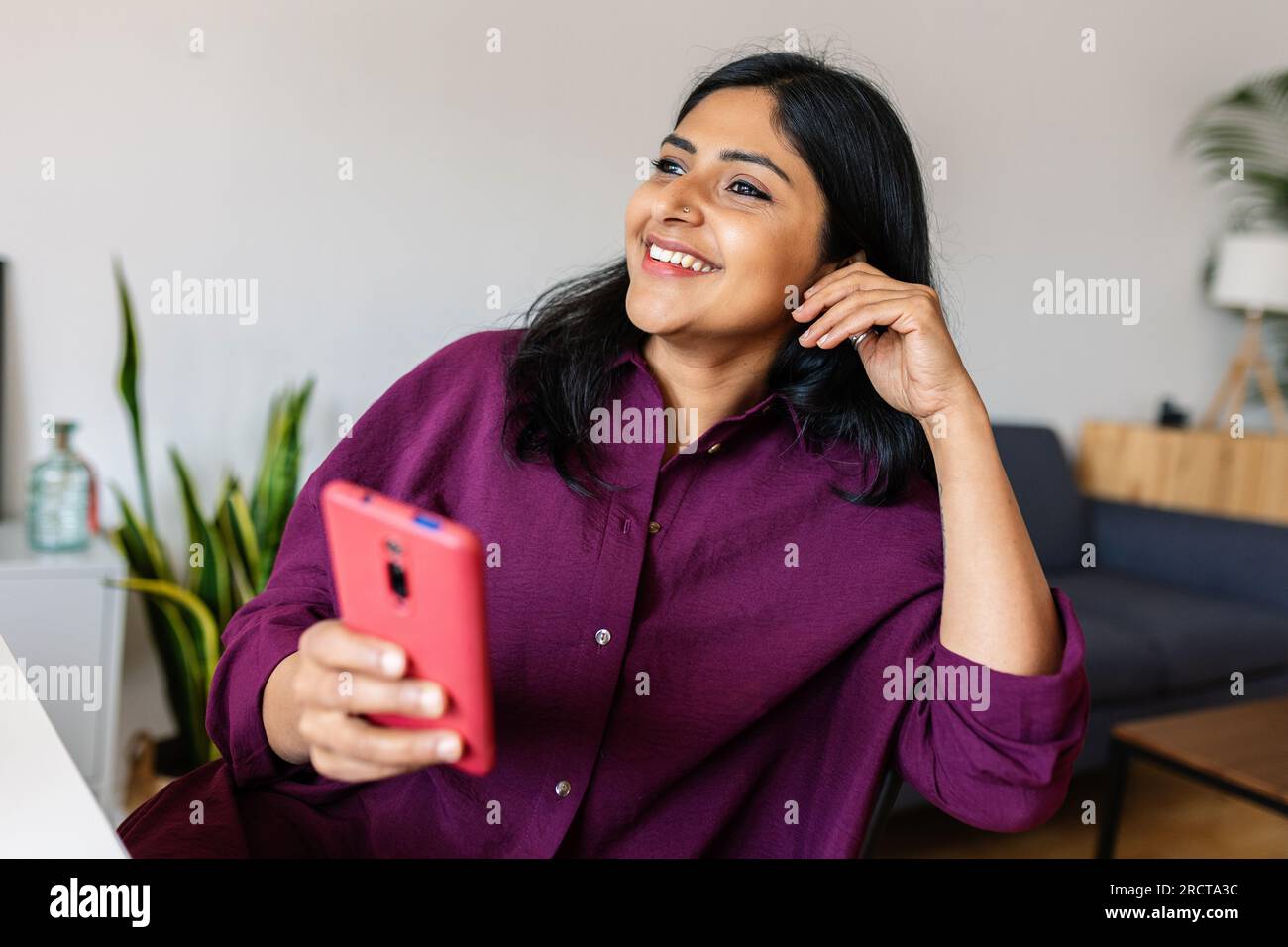 Glückliche, entspannte junge indische Frau, die zu Hause Handy benutzt Stockfoto