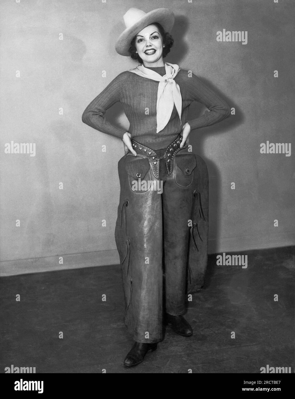 Vereinigte Staaten: c. 1940 eine attraktive Frau mit Cowboyhut, Taschentuch, Stiefeln und Männchen steht lächelnd mit den Händen auf der Hüfte. Stockfoto