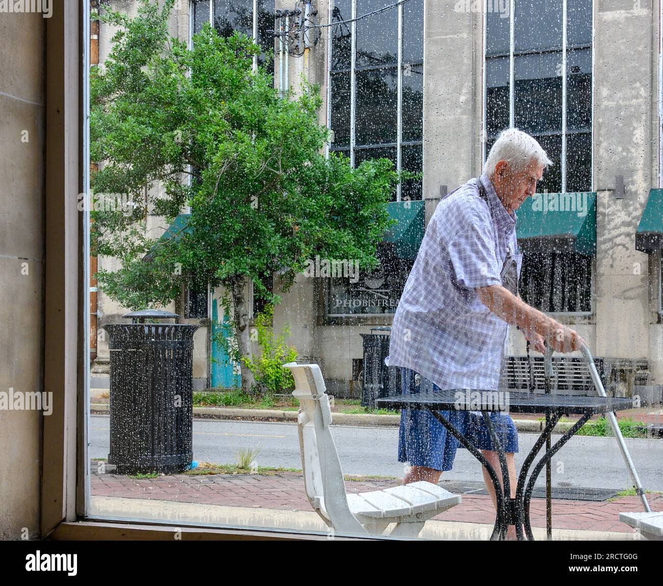 NEW ORLEANS, LA, USA - 12. JULI 2023: Männlicher Seniorenbürger, der mit zwei Stöcken am Fenster des Cafés in der Oak Street im Viertel Uptown vorbeigeht Stockfoto