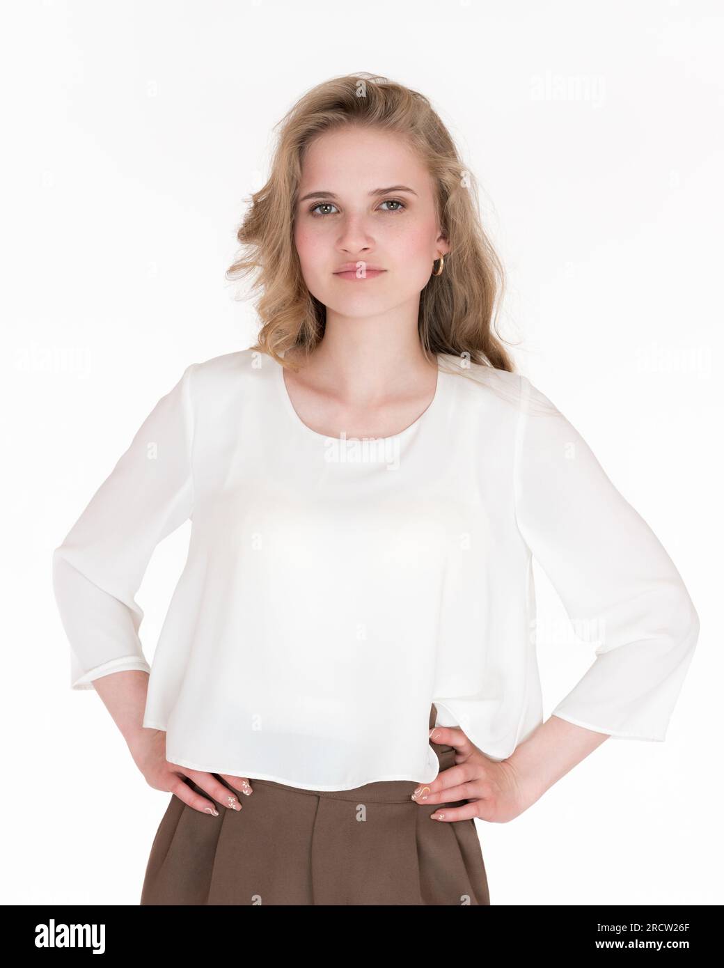 Charmante, blonde, weiße, junge Geschäftsfrau mit langen Haaren, die weiße Bluse und braune Hosen trägt. Europäische 21-jährige Frau, die in die Kamera schaut Stockfoto