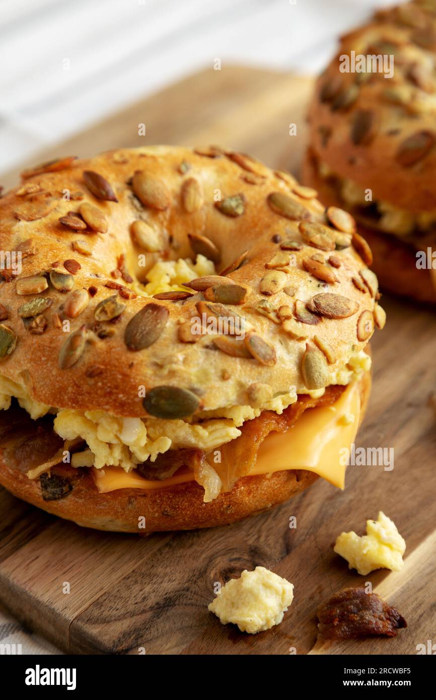 Hausgemachtes Bacon, Ei & Cheese Bagel Frühstückssandwich auf einem Holzbrett, Seitenansicht. Nahaufnahme. Stockfoto