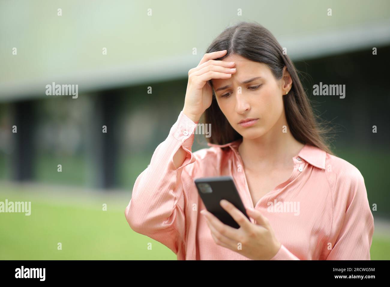 Besorgte Frau, die sich beschwert, um Nachrichten am Telefon in einem Park zu lesen Stockfoto