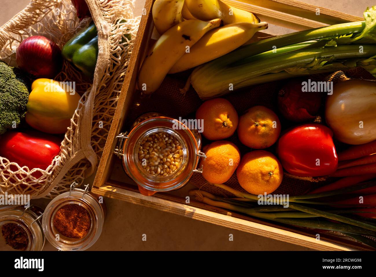 Frisches Gemüse, Obst und Getreide in der Kiste und wiederverwendbare Einkaufstasche auf der Theke in der sonnigen Küche Stockfoto