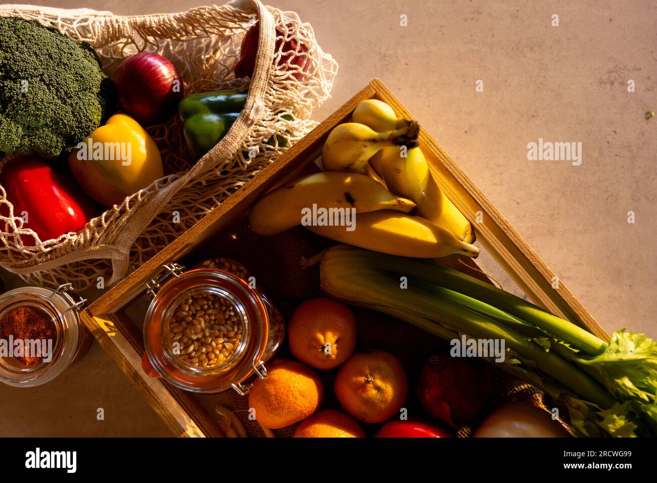 Frisches Gemüse, Obst und Getreide in der Kiste und wiederverwendbare Einkaufstasche auf der Theke in der sonnigen Küche Stockfoto