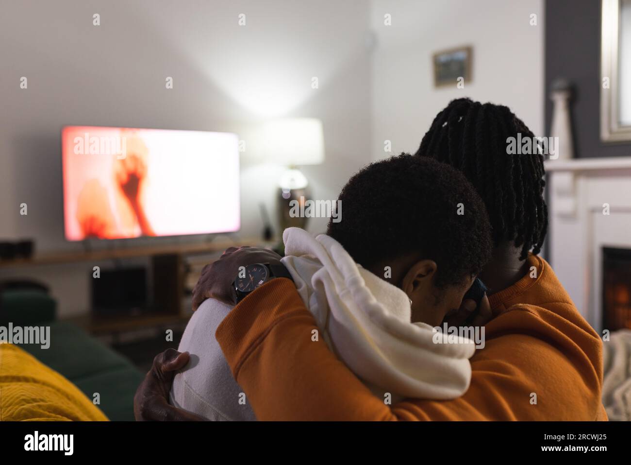 Ein afroamerikanisches Paar, das sich zu Hause entspannt, verängstigt ist, sich umarmt, sich einen gruseligen Film ansieht Stockfoto