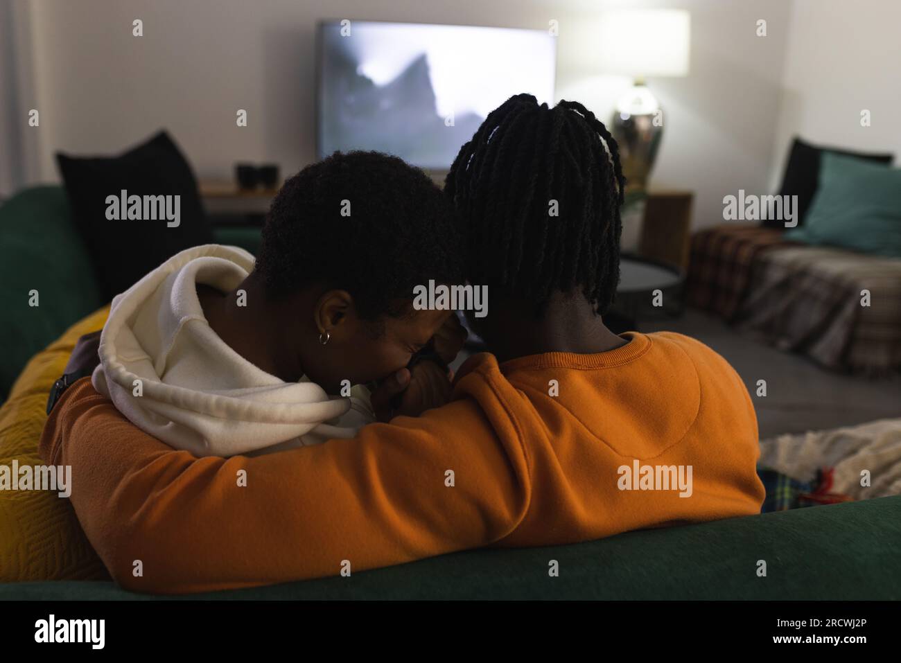 Ein afroamerikanisches Paar, das sich zu Hause entspannt, verängstigt ist, sich umarmt, sich einen gruseligen Film ansieht Stockfoto