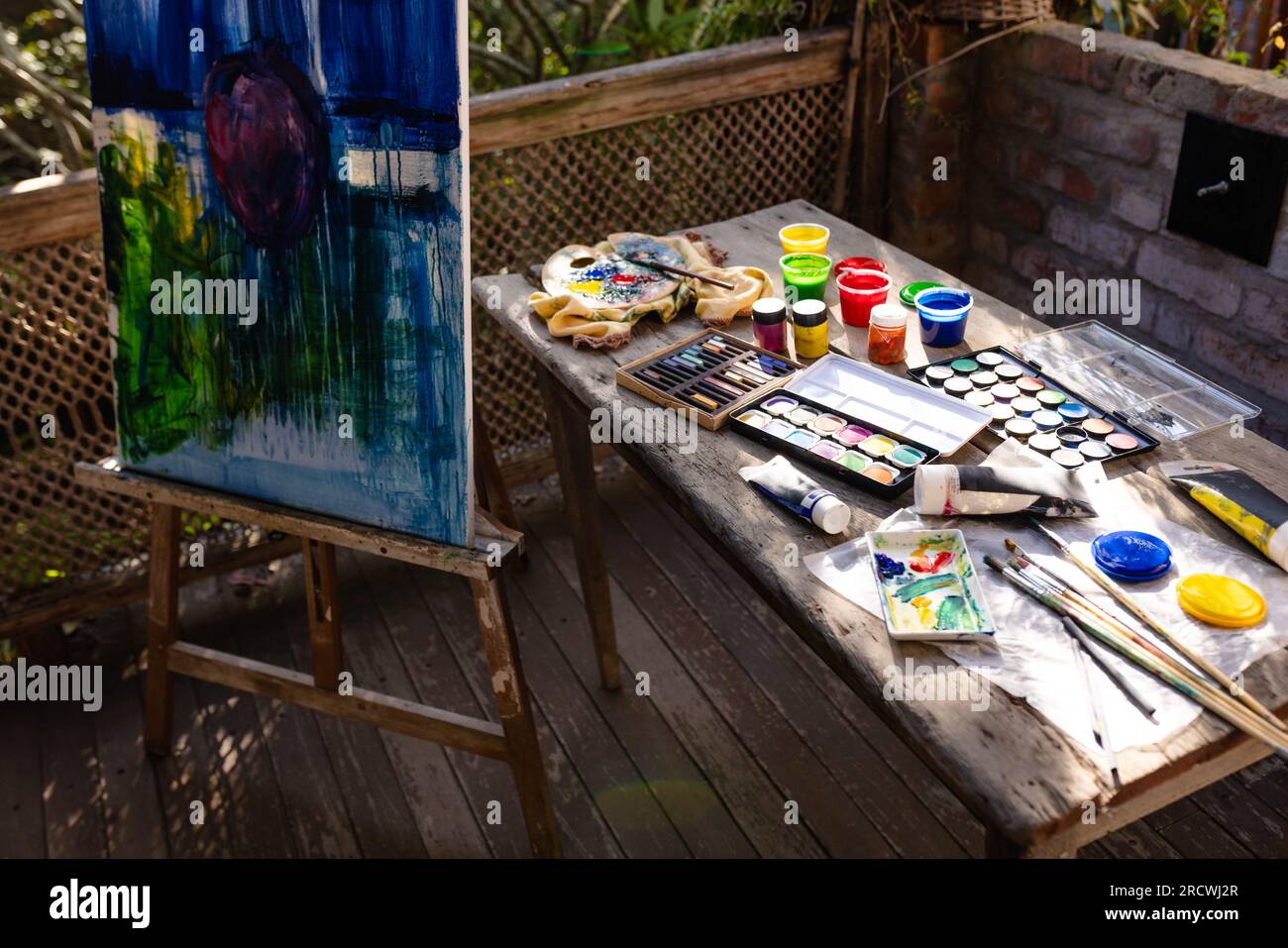 Nahaufnahme der Staffelei mit Malerei und Tisch mit Malgeräten auf der Terrasse Stockfoto