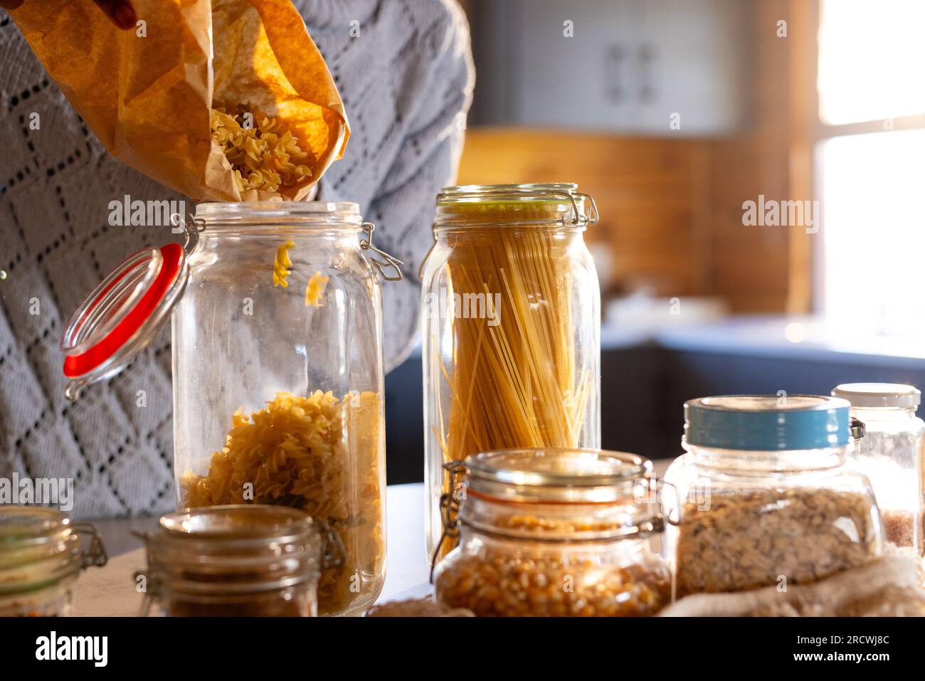 Eine afroamerikanerin, die Nudeln aus der Tüte in die Vorratsdose in der Küche gießt, Kopierraum Stockfoto