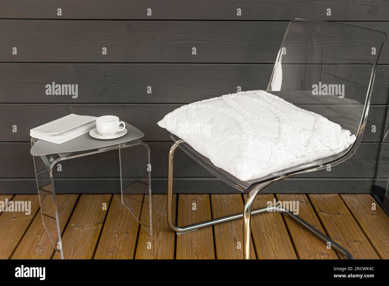 Klare, transparente moderne Acrylmöbel in Ihrem Zuhause. Stuhl mit Kissen, Beistelltisch mit Teetasse und Buch. Konzept alternativer Möbelmaterialien. Stockfoto