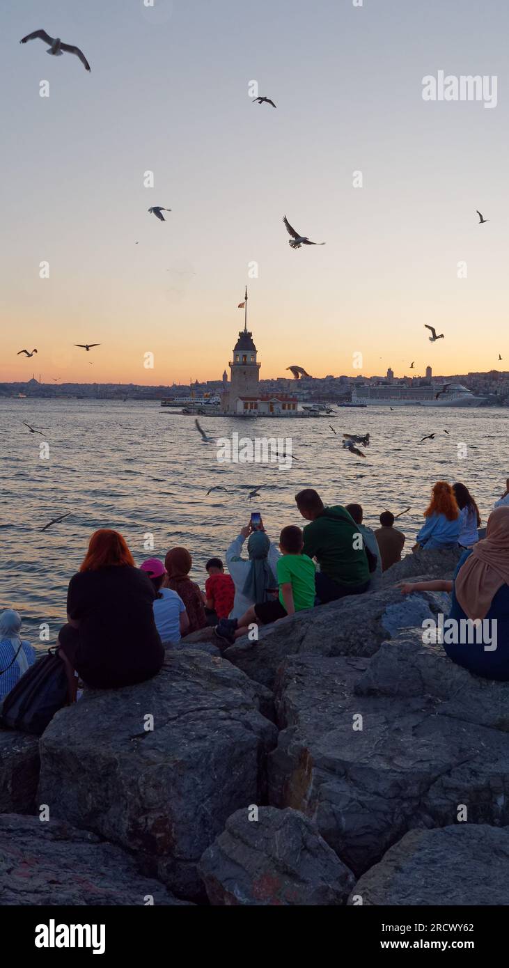 Die Menschen sitzen auf den Felsen und genießen den Sommeruntergang über dem Bosporus-Meer und dem Maidens-Turm von Uskudar auf der asiatischen Seite von Istanbul, Türkei Stockfoto