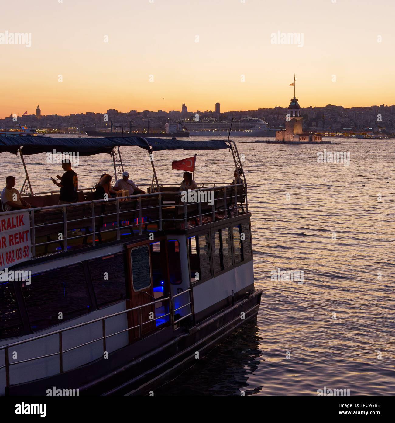 Menschen auf einem Boot genießen den Sonnenuntergang über dem Bosporus Meer und dem Maidens Tower von Uskudar, Istanbul, Türkei. Kreuzfahrtschiff hinten. Stockfoto