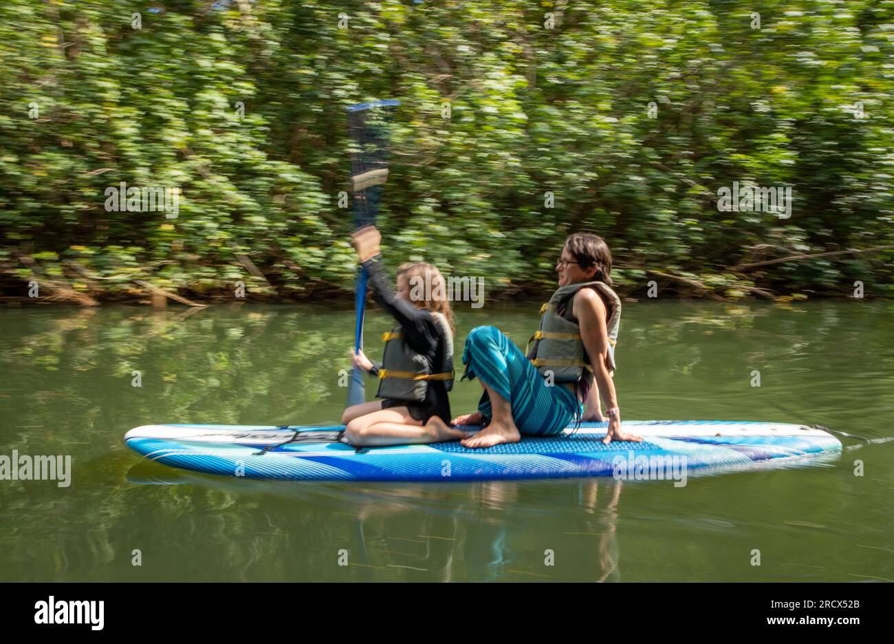 Mom sitzt hinter der Tochter auf dem Paddelbrett auf dem tropischen Fluss Stockfoto