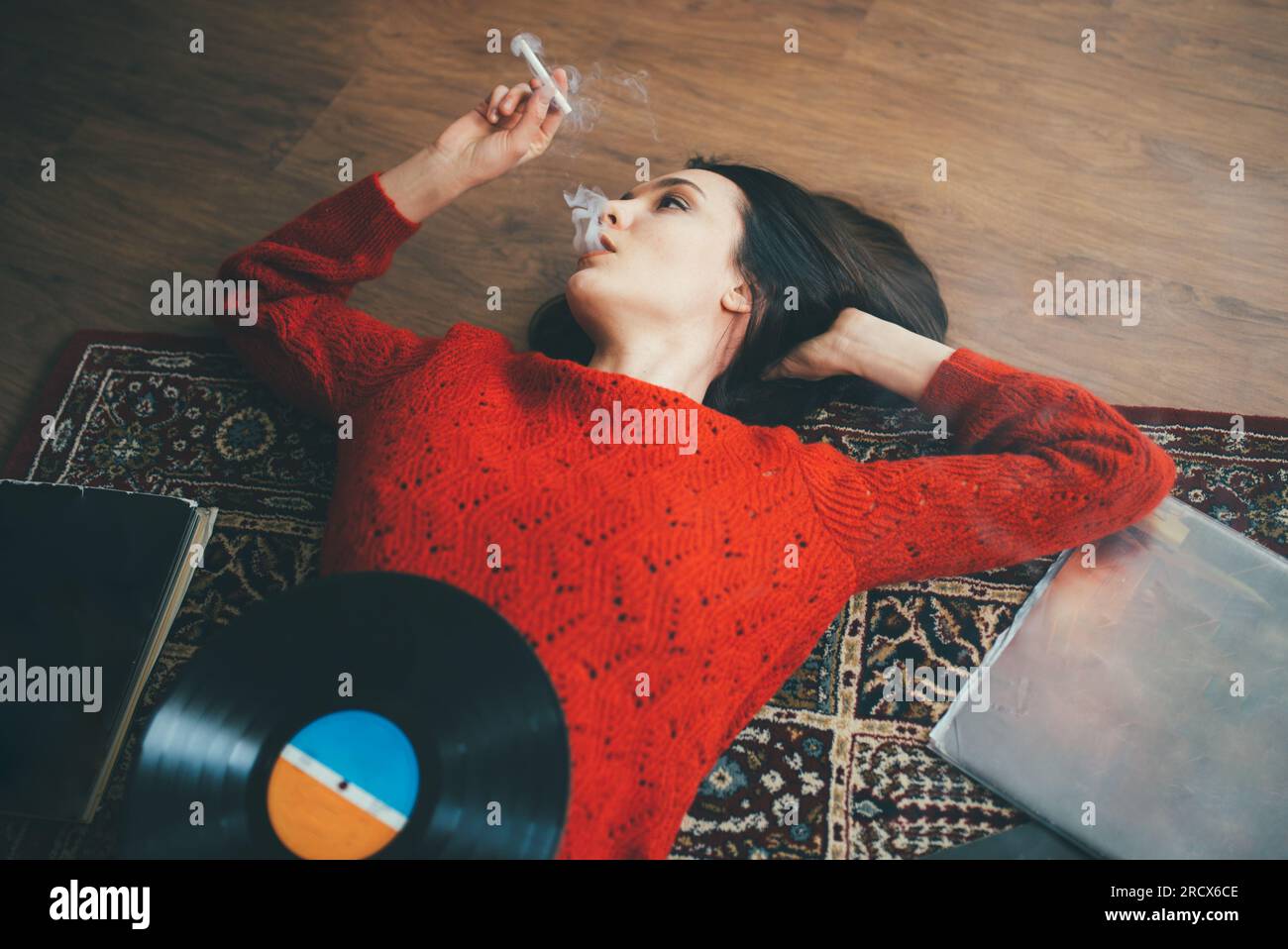 Frau lag auf dem Boden mit Vinyl, Büchern und rauchender Zigarette. Stockfoto
