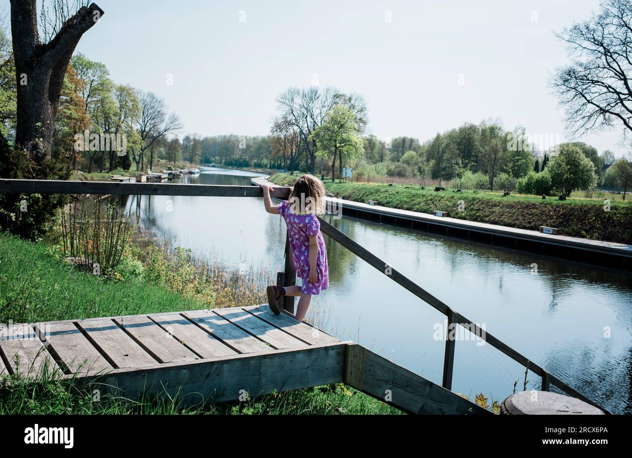 Ein junges Mädchen, das auf einem Steg steht und auf das Wasser schaut Stockfoto
