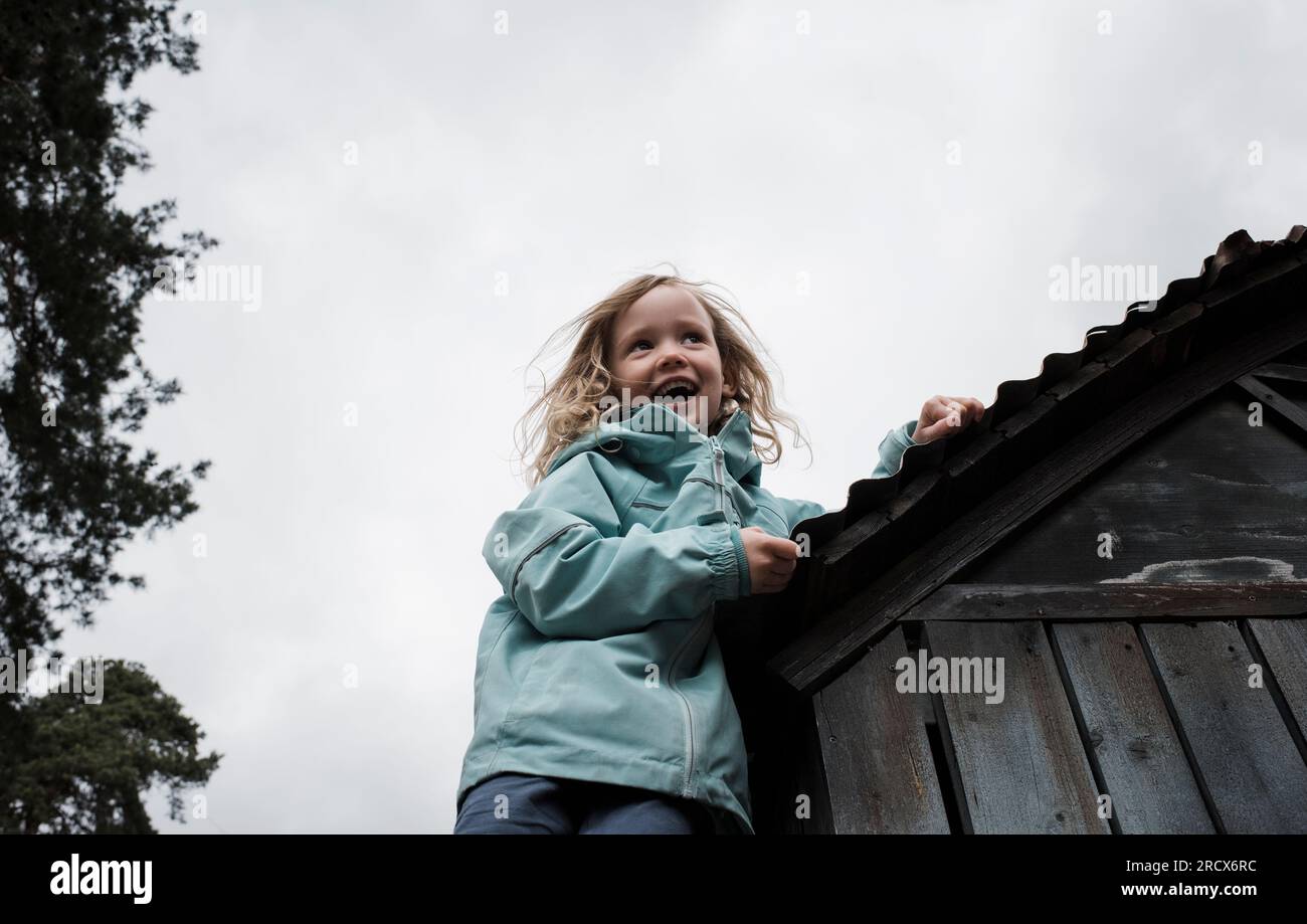 Ein junges Mädchen, das lächelt, während es draußen auf einen Schuppen klettert Stockfoto