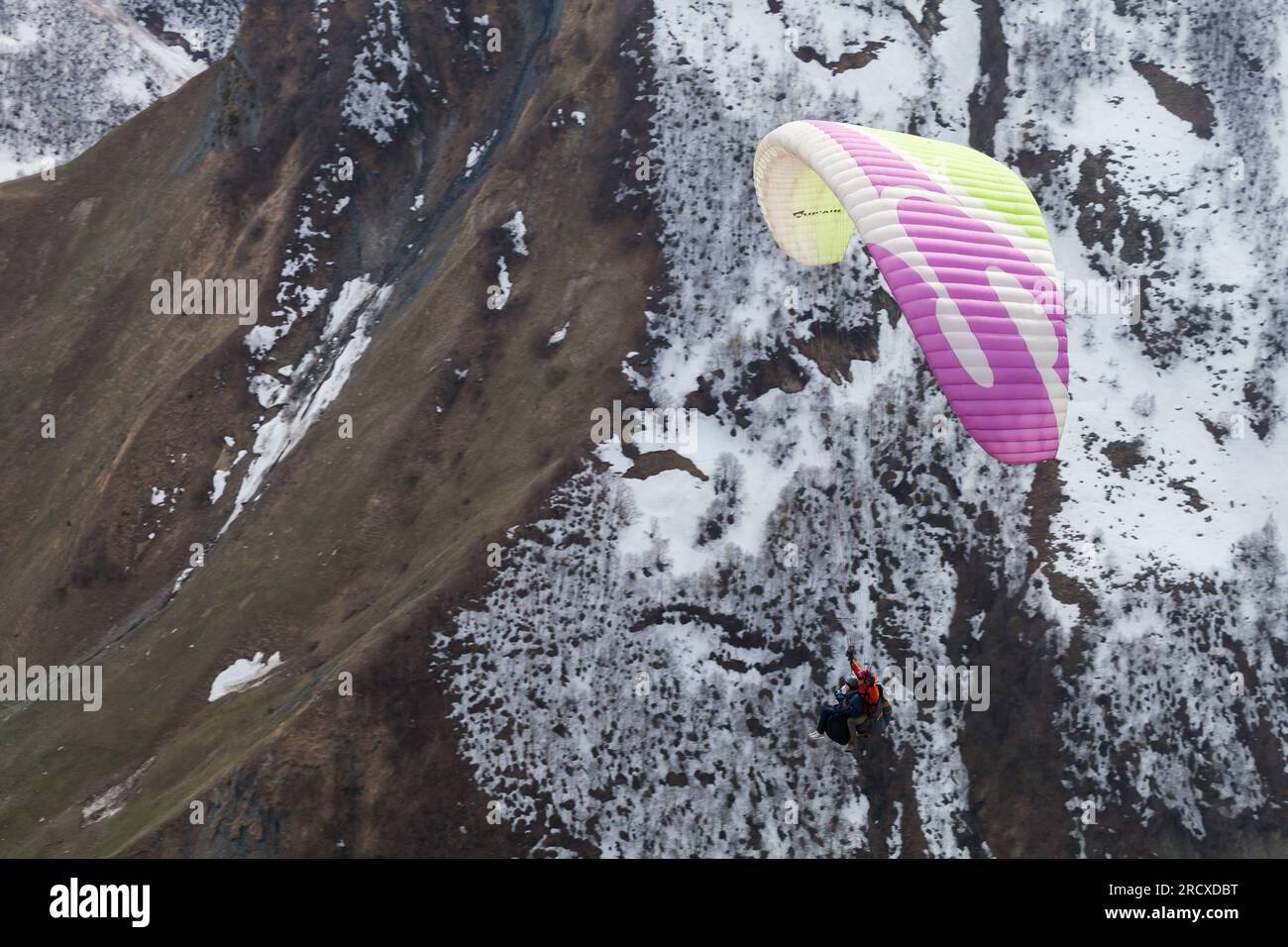 Gudauri, Georgia - 1. Mai 2019: Berglandschaft mit Gleitschirmfliegen vor den schneebedeckten Gipfeln des Kaukasus an einem Tag Stockfoto