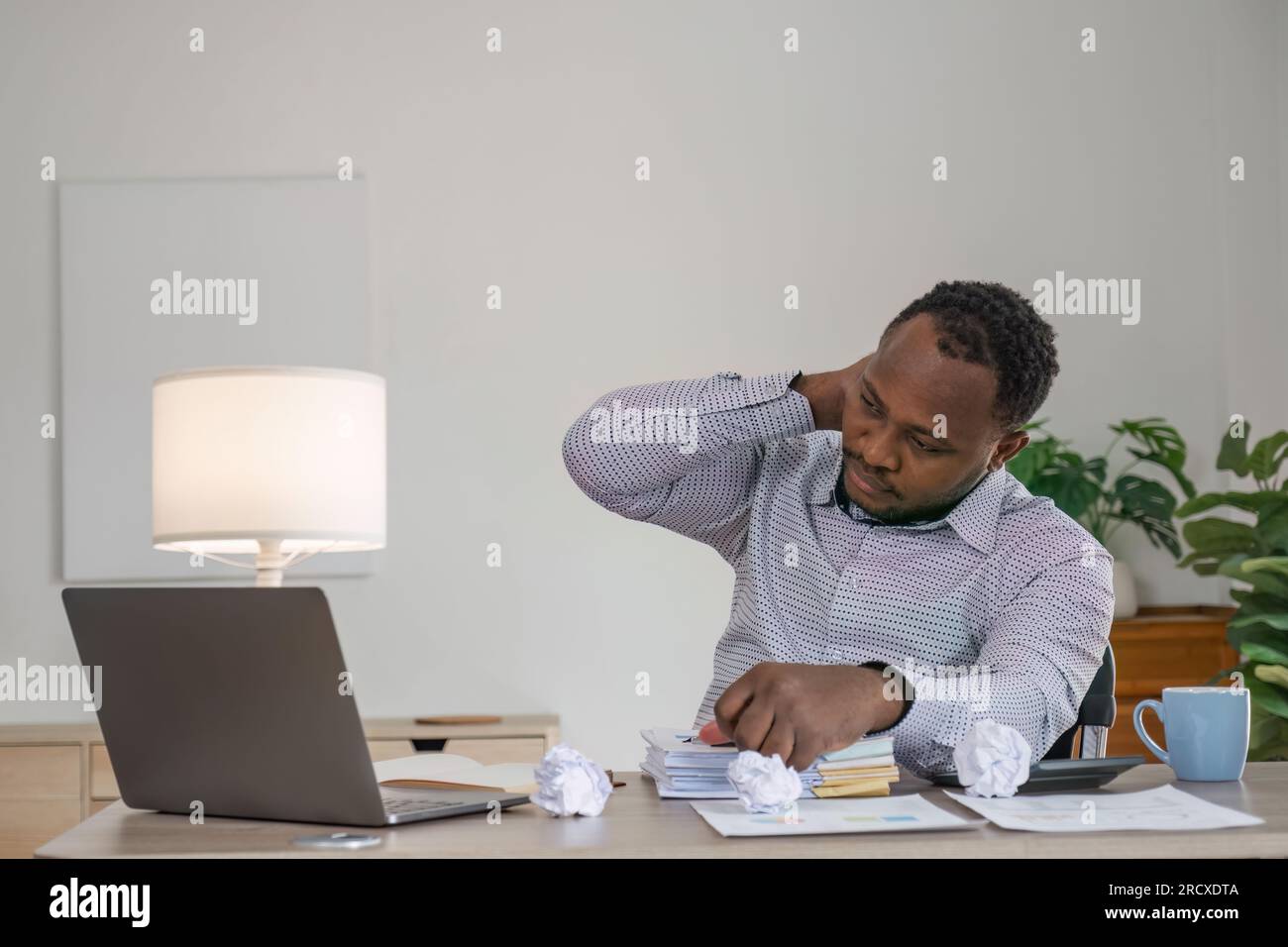 Müde, depressiv, gelangweilt, afrikanischer Geschäftsmann wegen Firmenversagen, Bankrott, wenn er sich ein Notebook ansieht, erschöpft, Kopfschmerzen, gestresstes schwarzes Büro Stockfoto