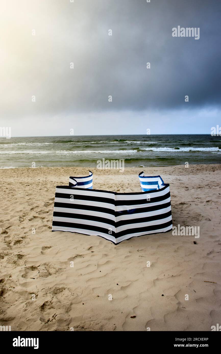 Windschutz. An einem bewölkten Tag am Strand, in der Hoffnung auf Sonnenschein. Vertikaler Rahmen. Wolken und Mai und ein gestreifter Strandschirm. Stockfoto