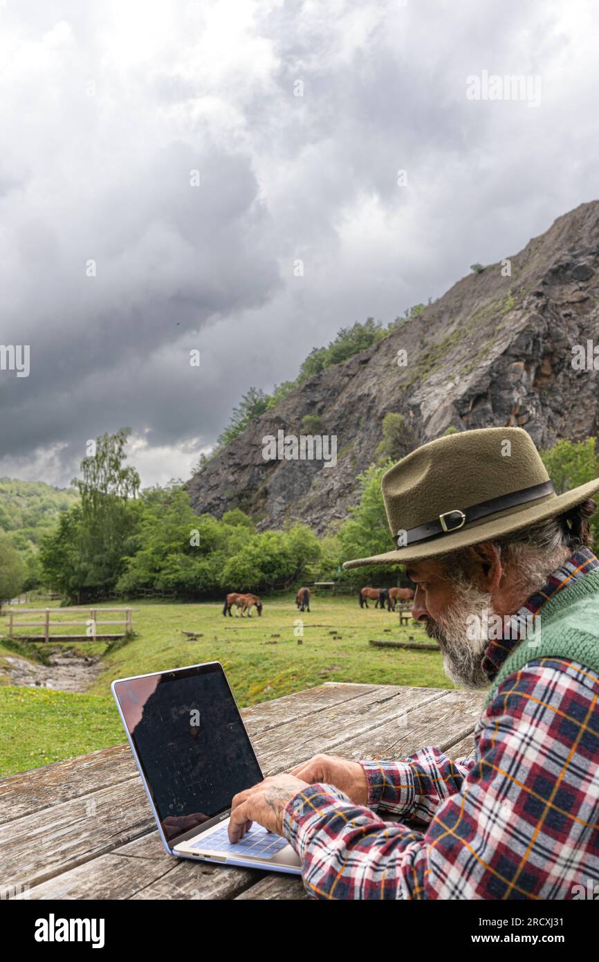 Freiberufler mit Hut, der überall online mit einem Laptop arbeitet und den Blick auf die Berge genießt Stockfoto