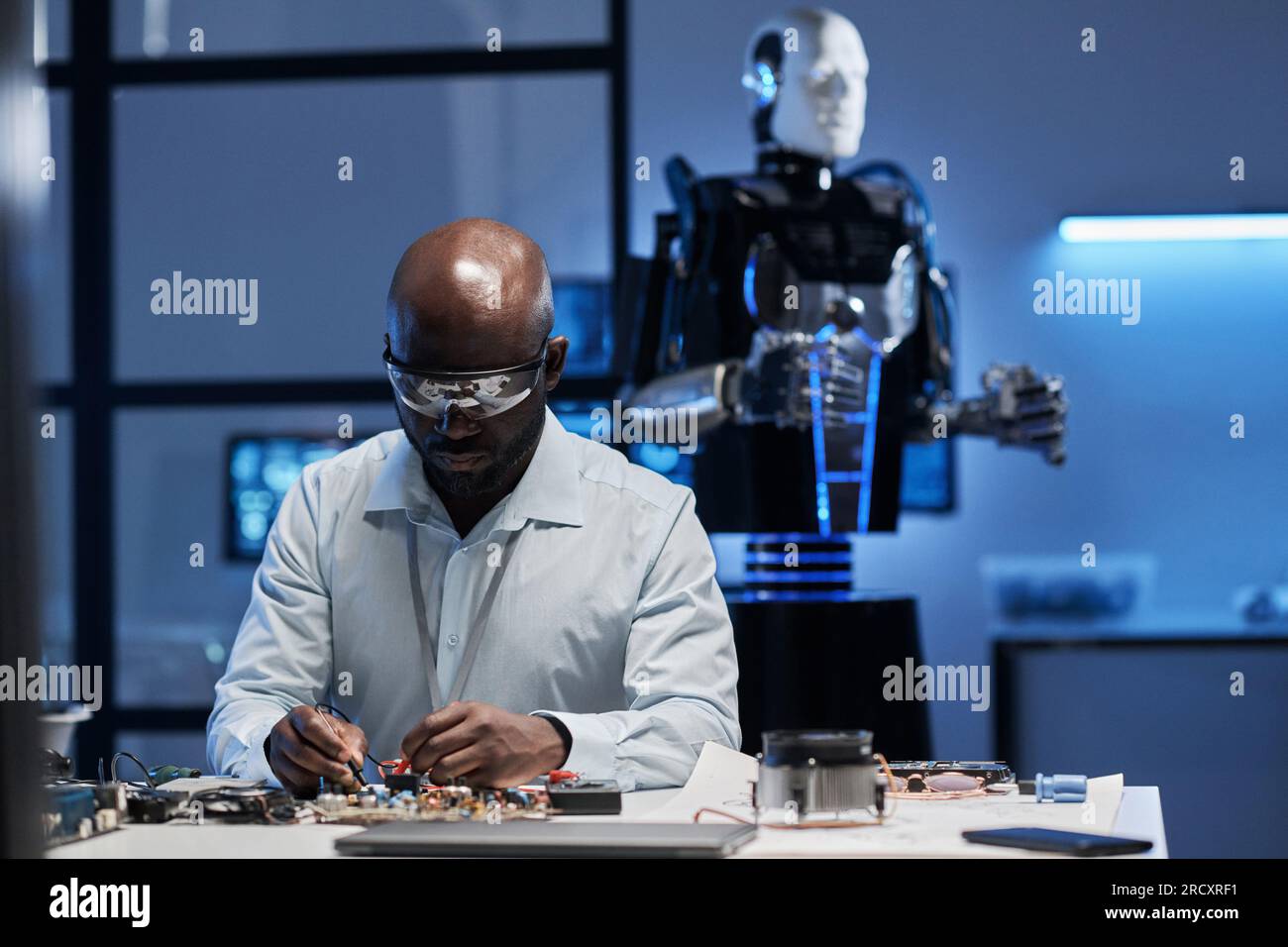 Afroamerikanischer Ingenieur für die Laborbeschichtung der Hauptplatine am Tisch im Labor Stockfoto