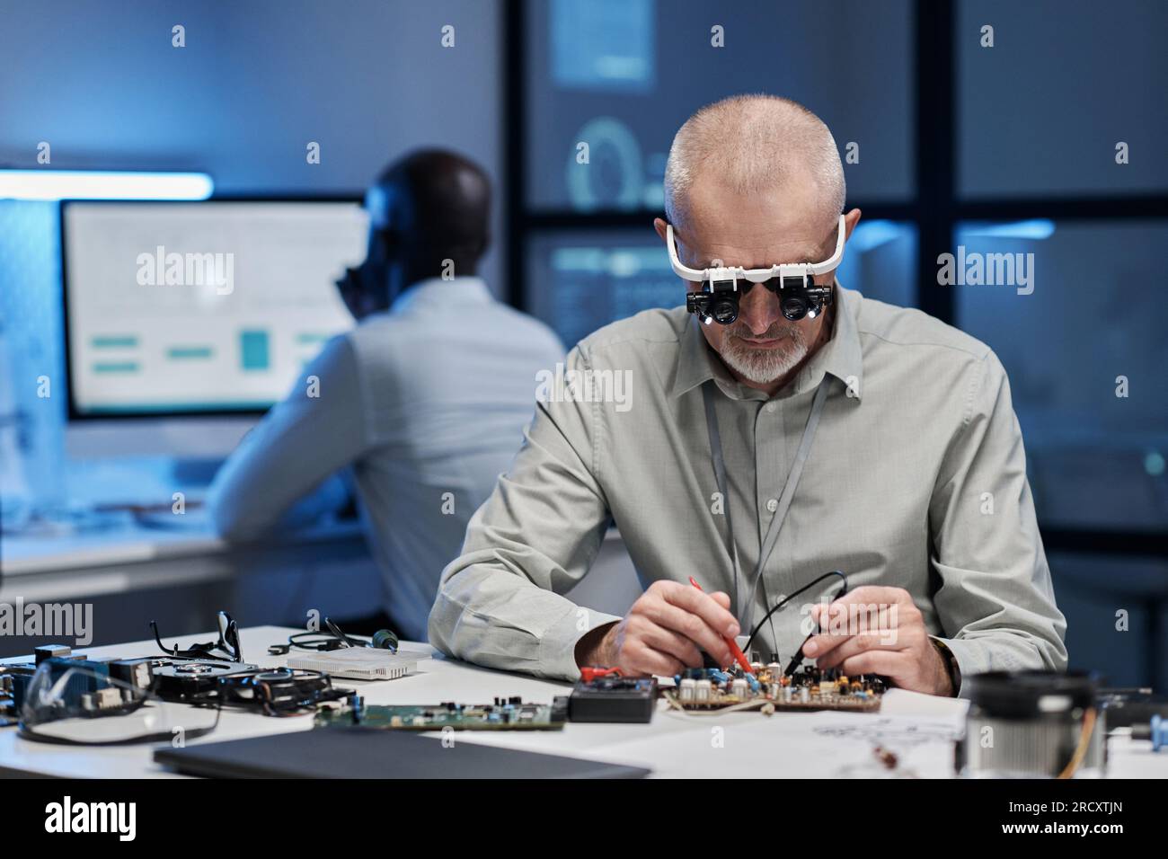 Erfahrener Ingenieur in Spezialgläsern, der sich auf seine Arbeit mit einem Computerchip am Tisch im Labor konzentriert Stockfoto