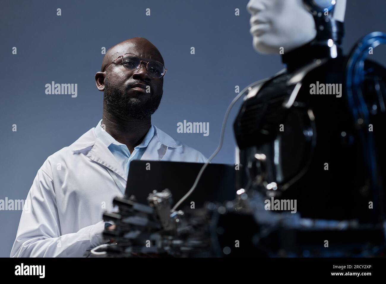 Ein afroamerikanischer Ingenieur untersucht die künstliche Intelligenz eines Roboters mit Laptop im Labor Stockfoto