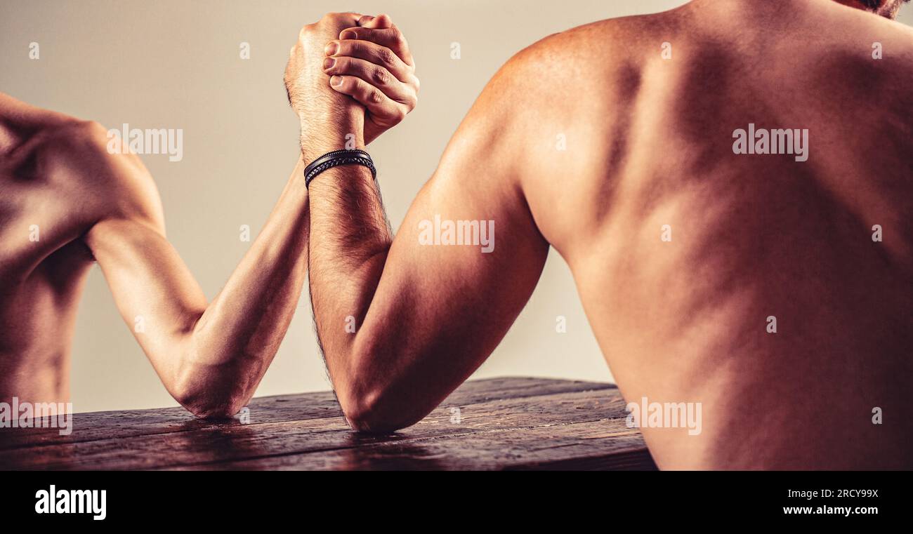 Die Hände zweier Männer umklammerten Arm-Wrestling, stark und schwach, ungleiche Übereinstimmung. Armdrücken. Kräftig muskeliger, bärtiger Arm, der mit einem schwachen Mann kämpft Stockfoto