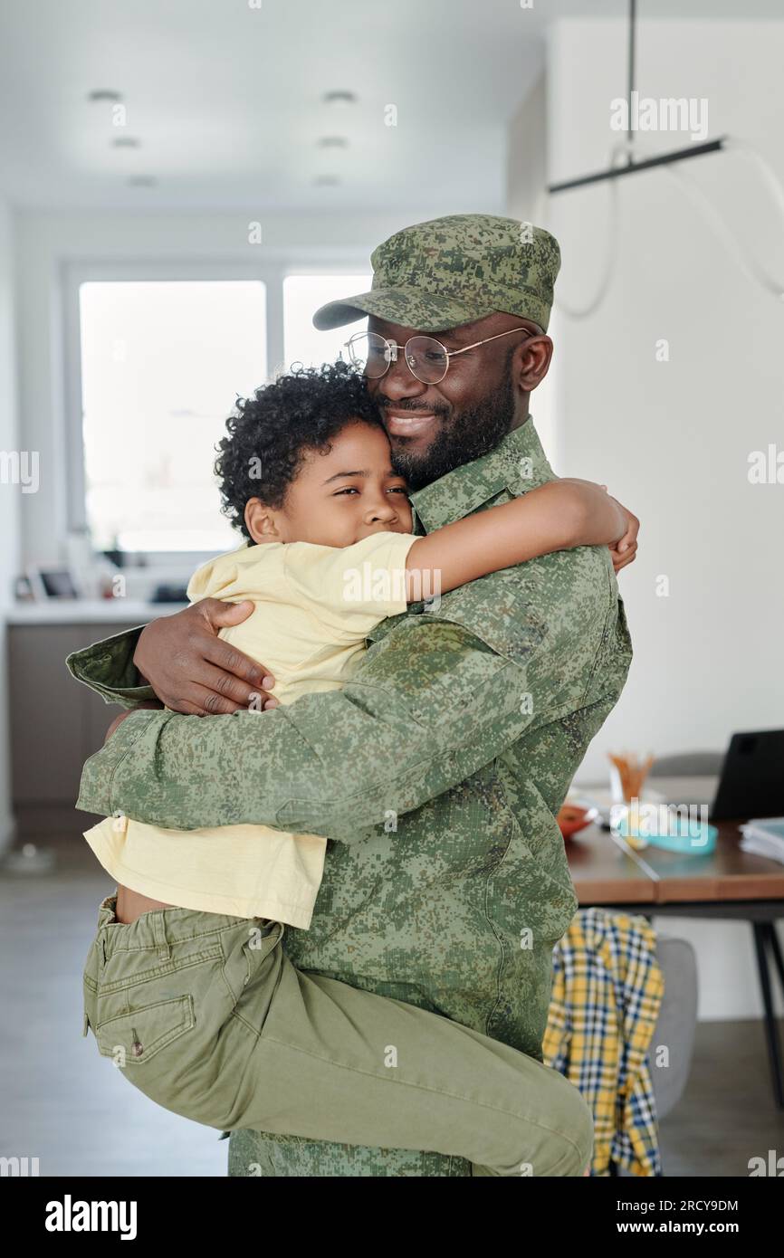 Vertikales Bild von dem kleinen Sohn, der seinen Vater in Militäruniform umarmt, er trifft ihn aus dem Krieg zu Hause Stockfoto