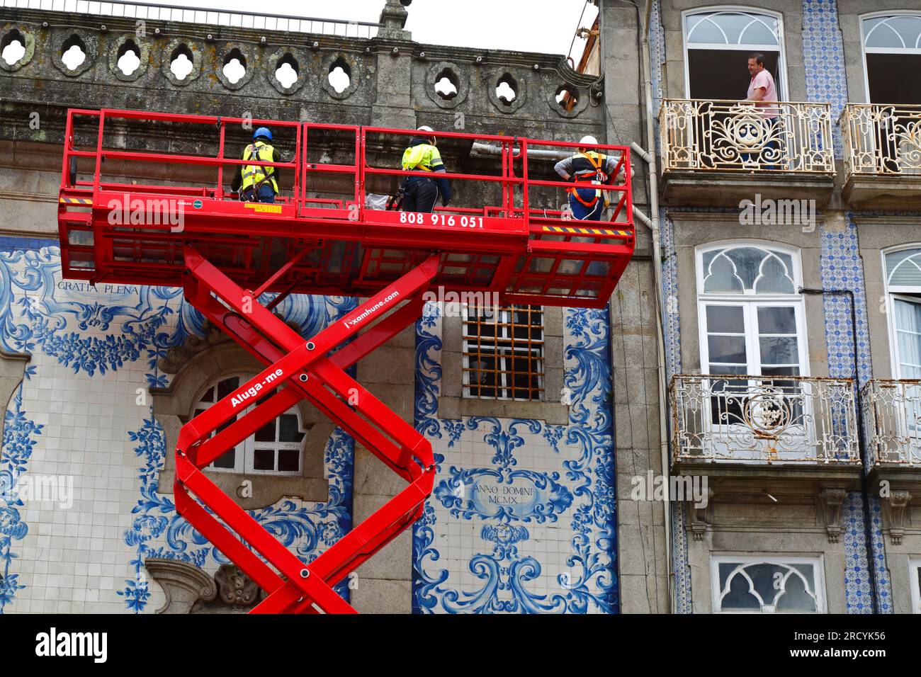 Ein Mann auf dem Balkon beobachtete Arbeiter auf einer erhöhten Scherenaufzugplattform bei der Wartungsinspektion der Igreja do Carmo Kirche, Porto/Porto, Portugal Stockfoto