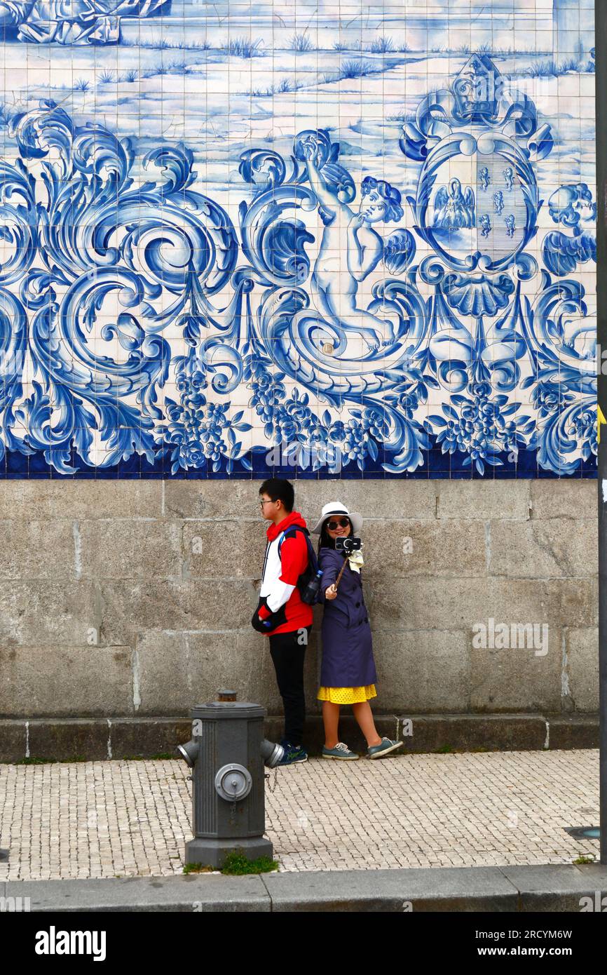 Ein junges asiatisches Paar macht ein Selfie vor den Asulejos/Keramikfliesen an der Seitenwand der Kirche Igreja do Carmo, Porto/Porto, Portugal Stockfoto