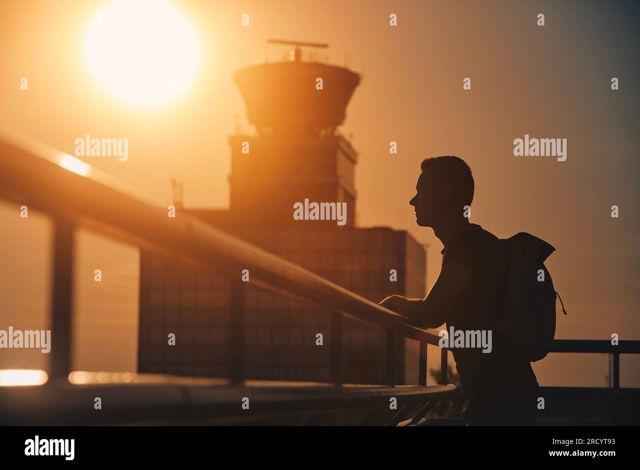 Reisender mit Rucksack am Flughafen. Silhouette des Menschen gegen den Flugverkehrskontrollturm bei Sonnenuntergang. Stockfoto