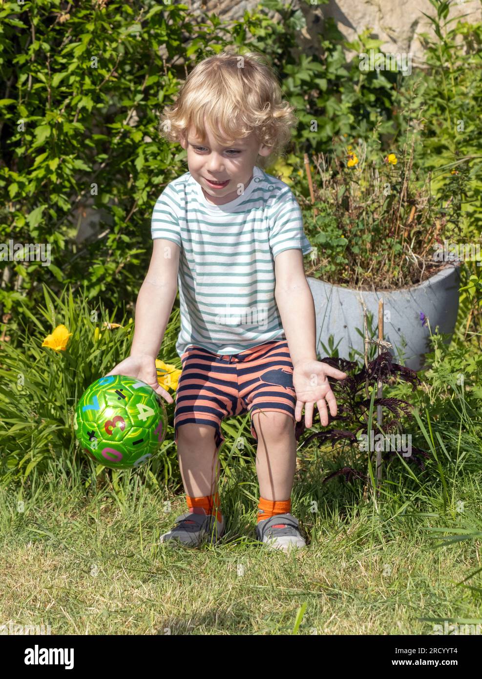 Ein kleiner Junge fängt einen Ball im Sommergarten Stockfoto
