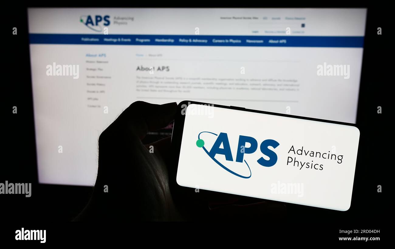 Person, die ein Mobiltelefon mit dem Logo der US-Organisation American Physical Society (APS) auf dem Bildschirm vor der Webseite hält. Konzentrieren Sie sich auf das Display des Telefons. Stockfoto