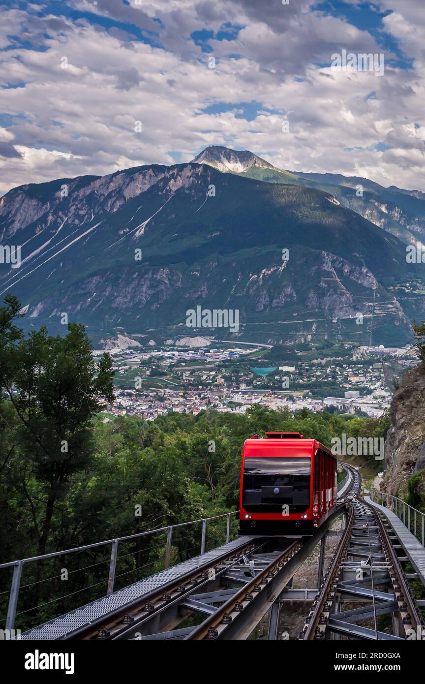 Eine rote Schweizer Standseilbahn von Sierre nach Crans Montana, Valais Kanton, Schweiz. Öffentliche Verkehrsmittel mit Seilbahn und malerischem Blick auf Sierre City und mou Stockfoto