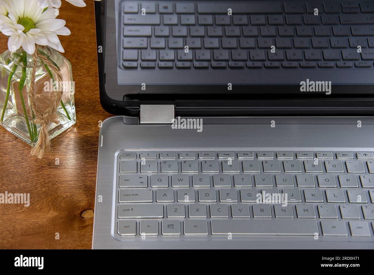 Nahaufnahme einer Laptop-Computer-Tastatur auf einem hölzernen Schreibtisch mit Gänseblümchen in einer Glasvase Stockfoto