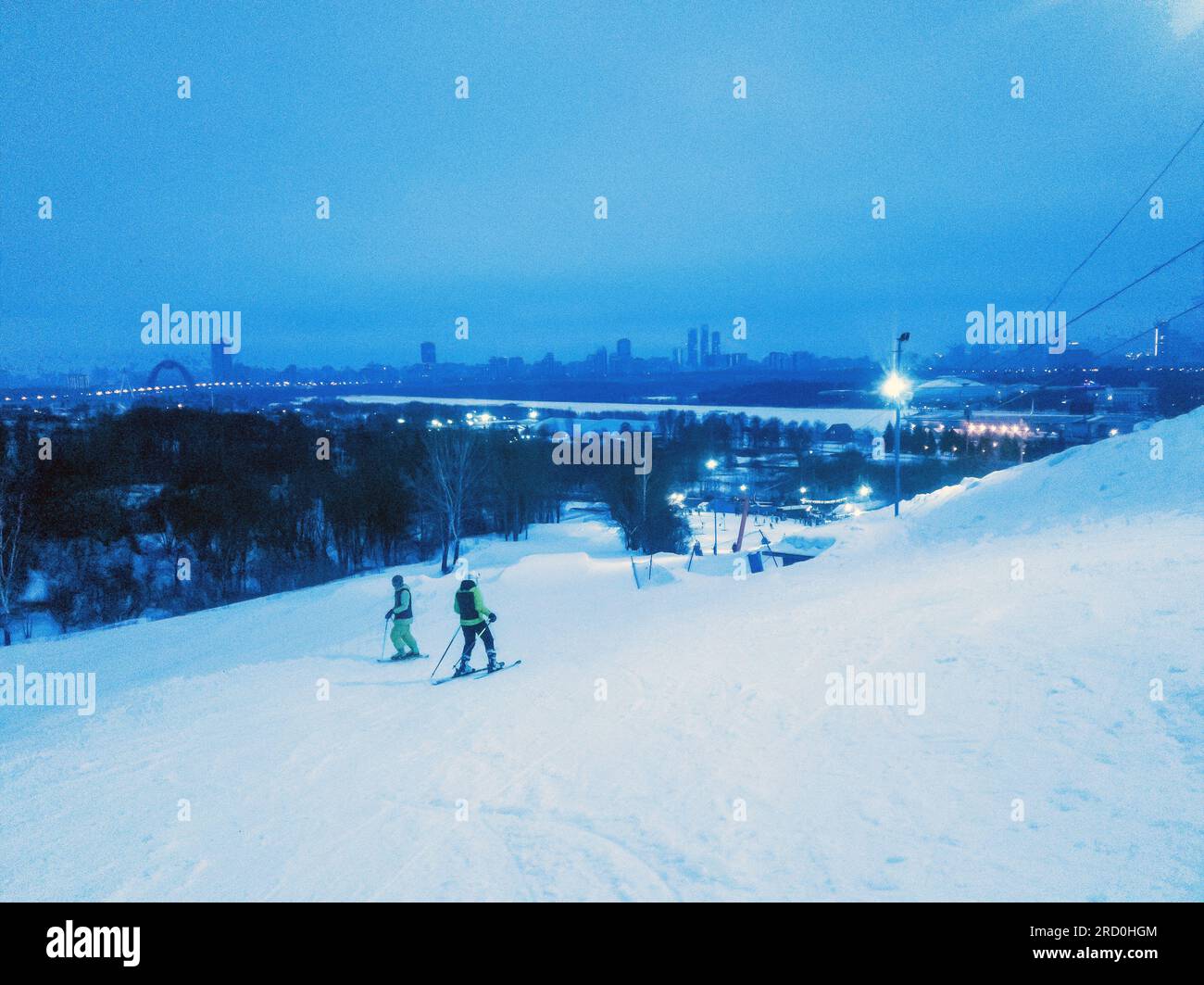 Beeindruckendes Panorama über Moskau bei Nacht und 2 Skifahrer (in der Ferne) auf der Piste des Skikomplexes Lata-Track. Zhivopistiy-Brücke in der linken und gefrorenen Moskva ri Stockfoto