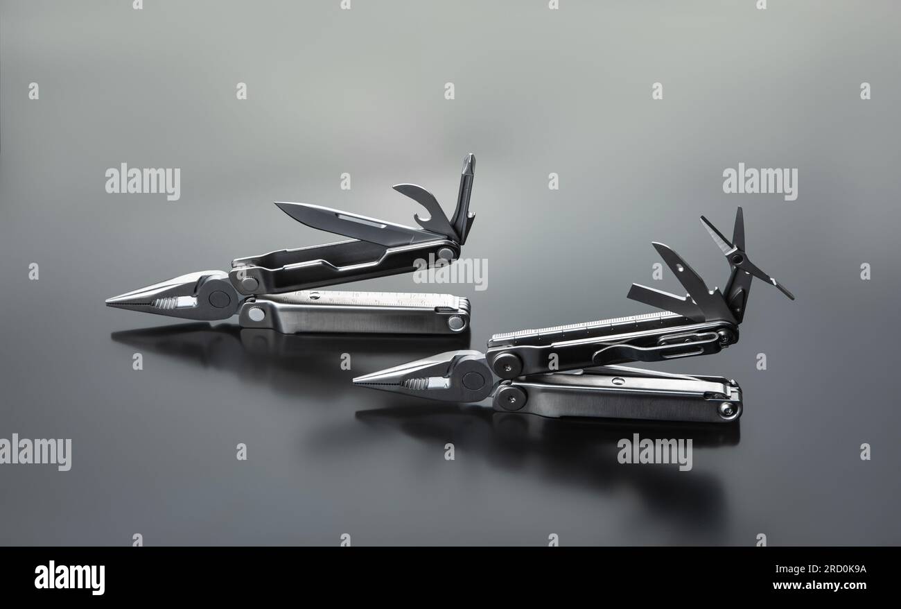 Zwei silberfarbene Multifunktionswerkzeuge mit Zange, Scherenmesser, Schraubendreher und Flaschenöffner. Vielseitiges Taschenwerkzeug. Hellgrauer Hintergrund. Stockfoto