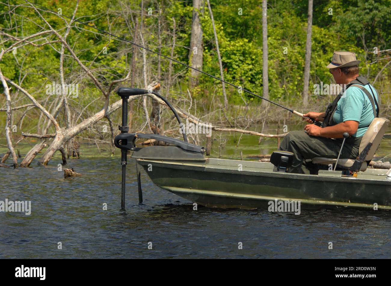 Reifer Mann fischt in einem südlichen Arkansas See. Er taucht in seinem Barschboot auf und schlängelt sich durch die Gewässer auf der Suche nach Fischen. Er trägt einen Overall und einen Hut. Stockfoto