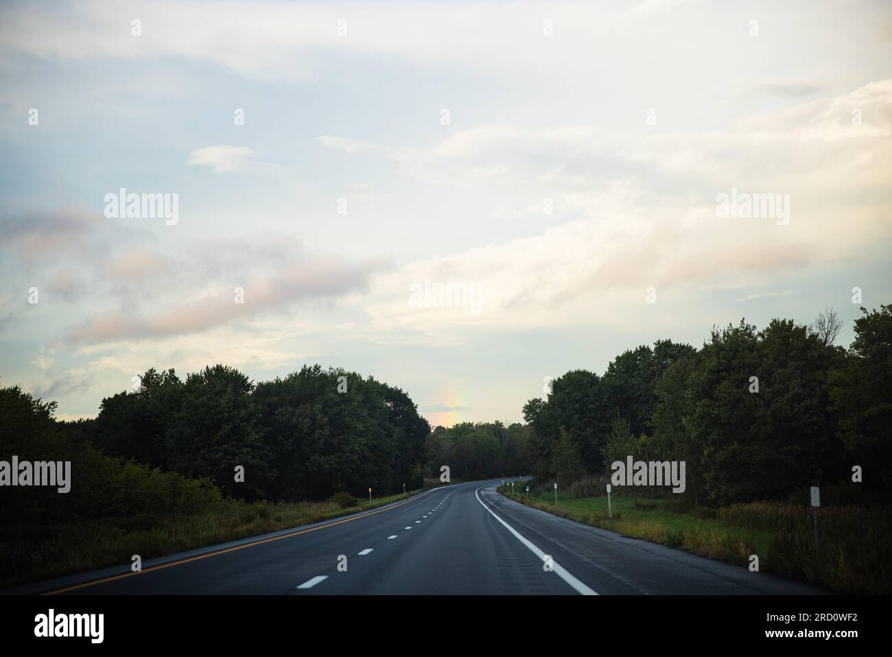 Eine Landschaft mit einem Anwesen am See, umgeben von Wäldern, die die Straße hinunter fahren, mit einem Regenbogen am Ende und Regentropfen auf der Fensterbank. Stockfoto