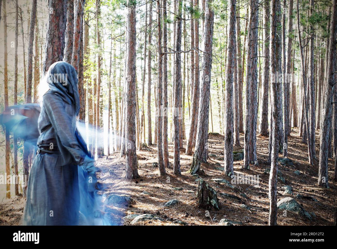 Eine Frau in einem Kapuzenkleid tanzt in einem magischen Wald. Das Foto erweckt eine überirdische Geisterqualität. Stockfoto